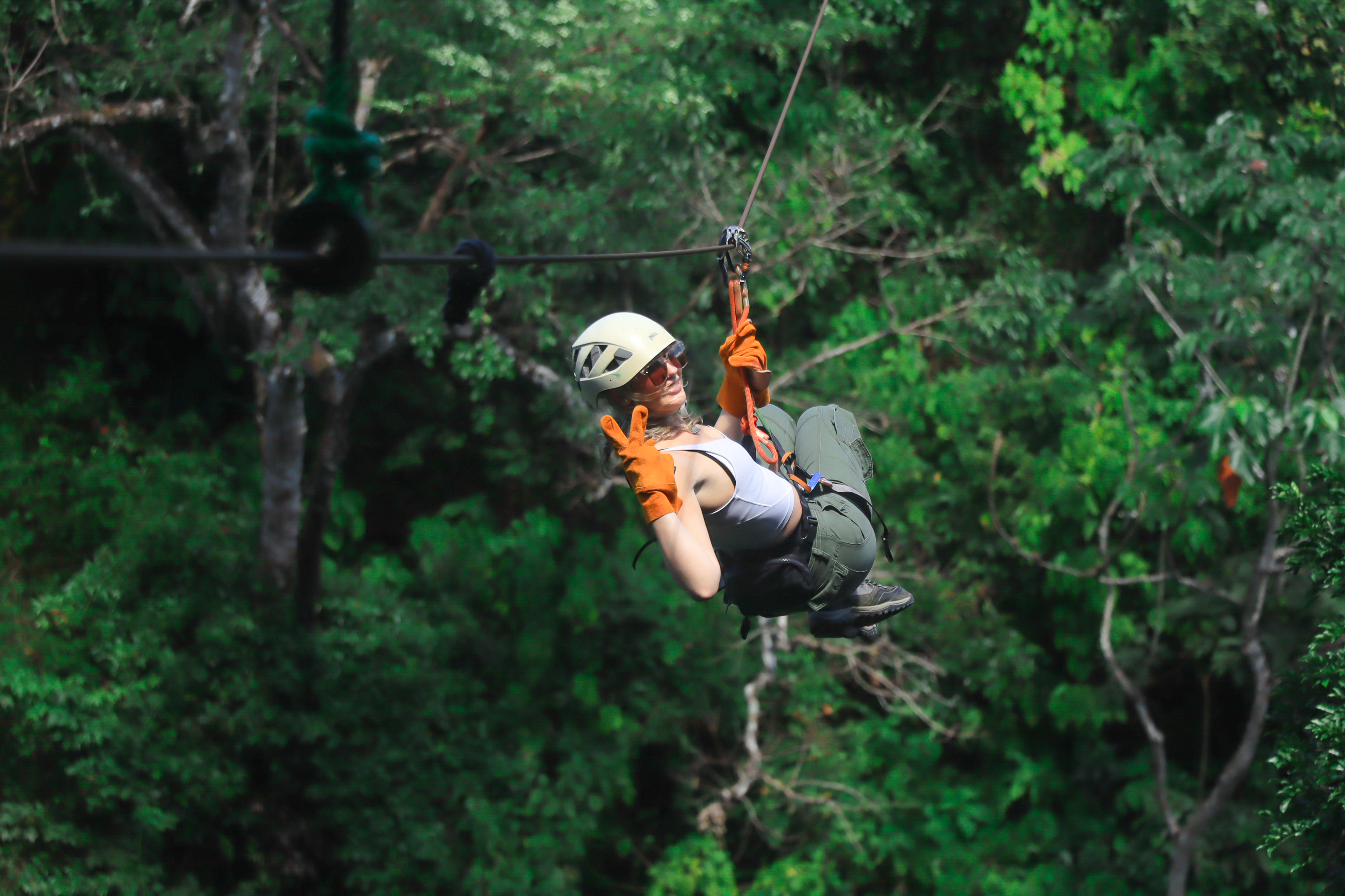 Person zip-lining through a forest, wearing a helmet and gloves.