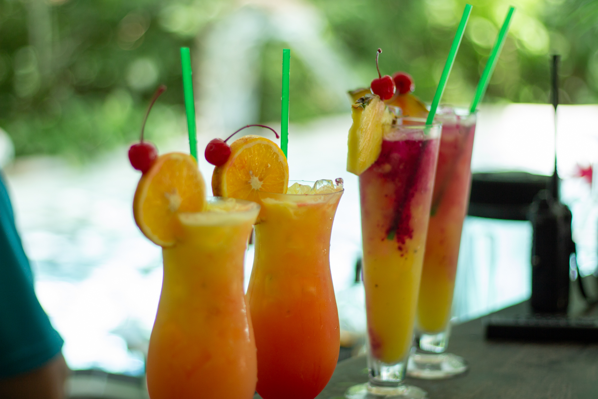 Bebidas tropicales coloridas con pajitas, adornadas con rodajas de naranja y cerezas en la barra de un bar.