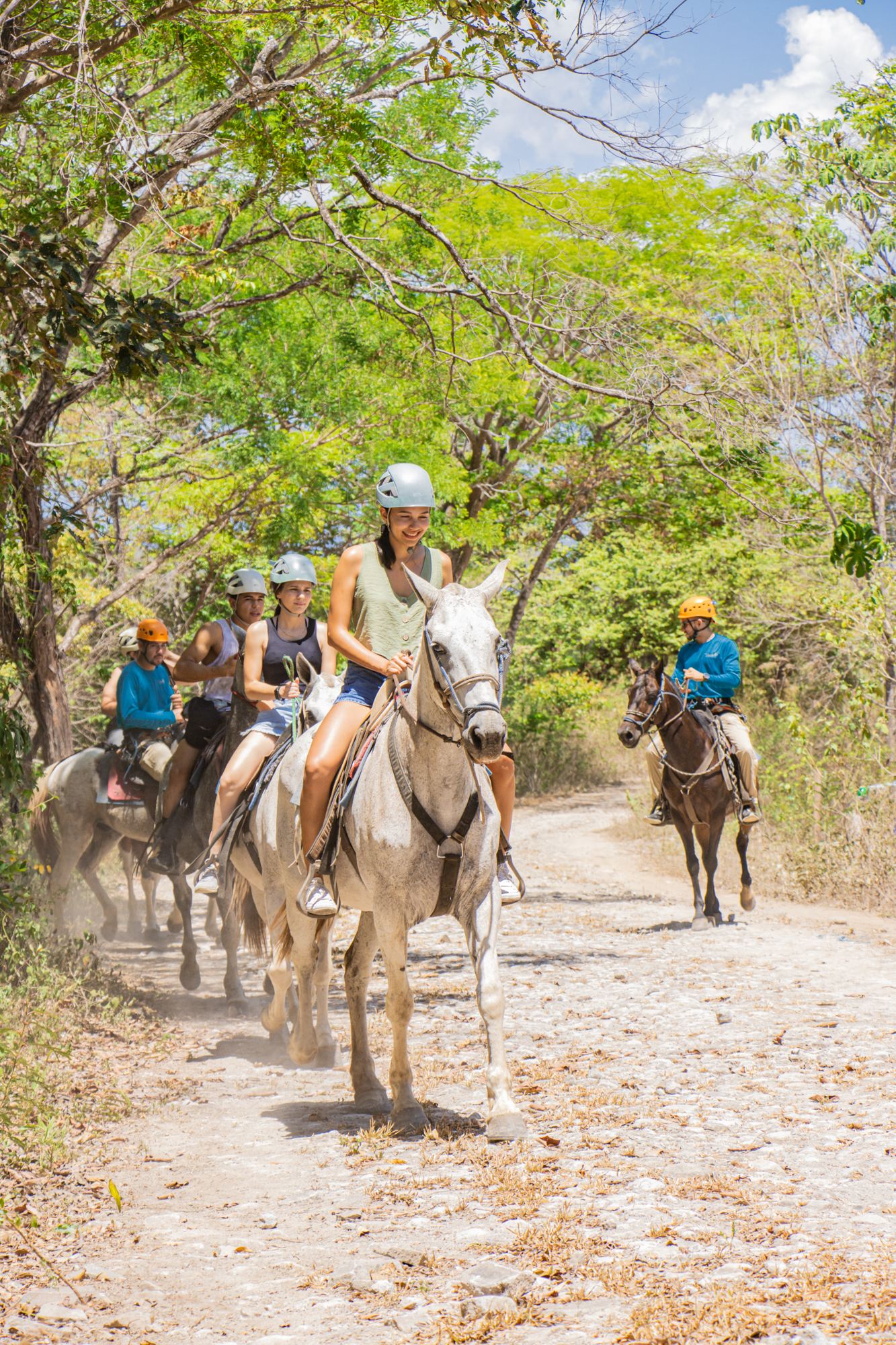 Grupo de personas montando a caballo por un sendero de tierra a través de una exuberante vegetación.