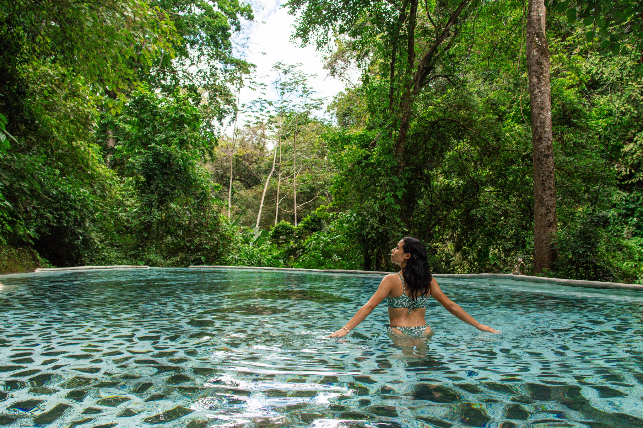 Persona en una piscina rodeada de un exuberante bosque verde.