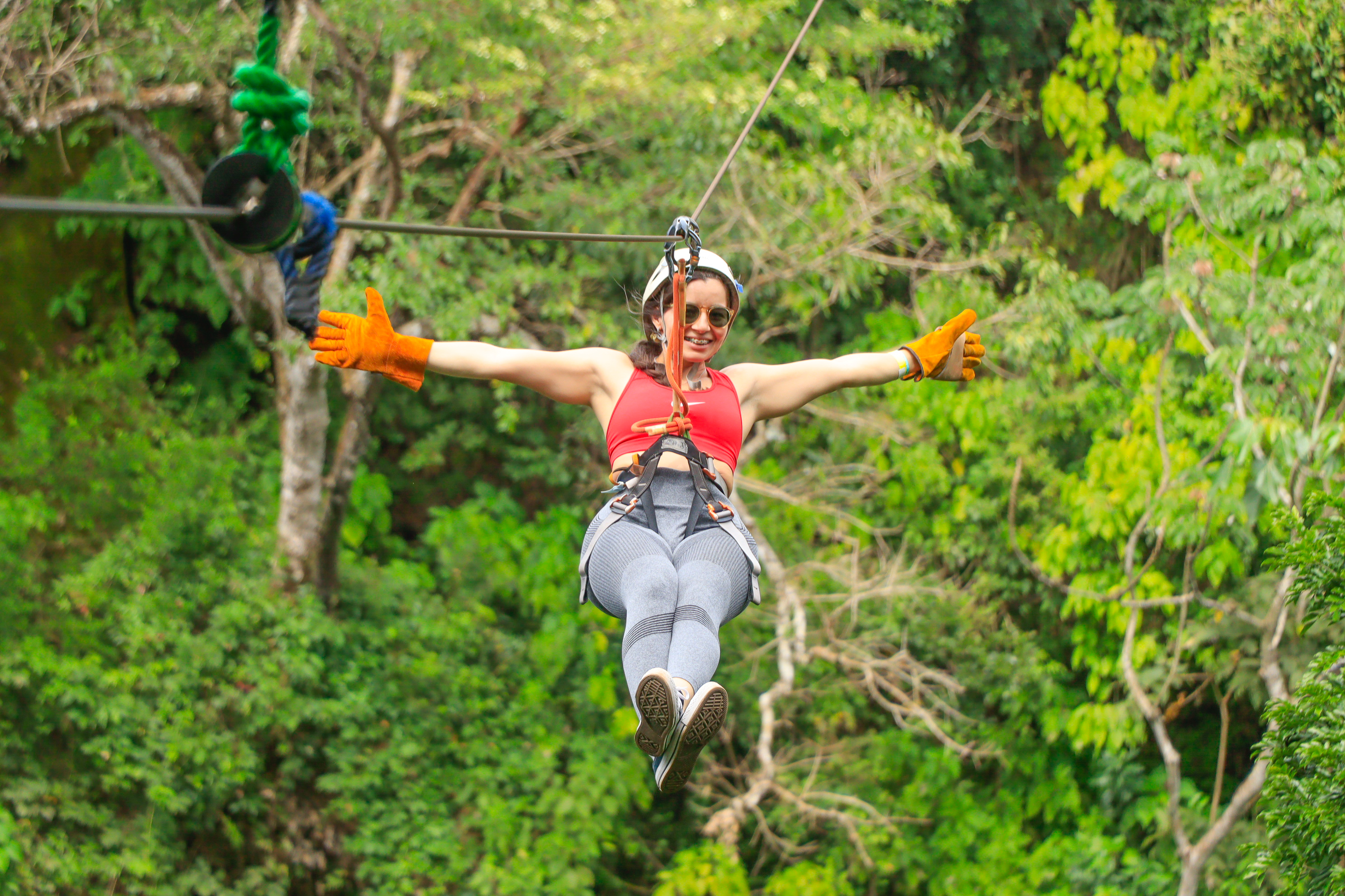 Persona haciendo tirolina por el bosque con los brazos extendidos, usando guantes y arnés.
